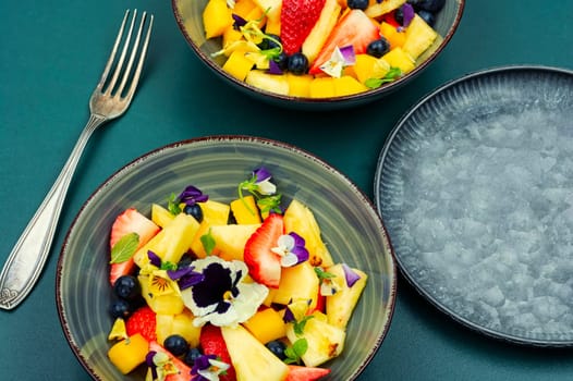 Salad of pineapple, strawberries and berries with edible flowers in a bowl