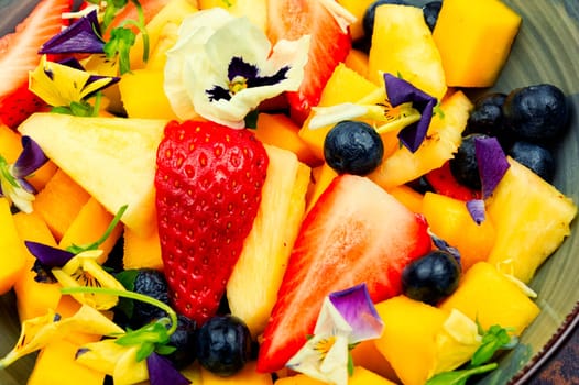 Salad of pineapple, strawberries and berries with edible flowers in a bowl