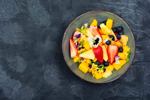 Salad of pineapple, strawberries and berries with edible flowers in a bowl