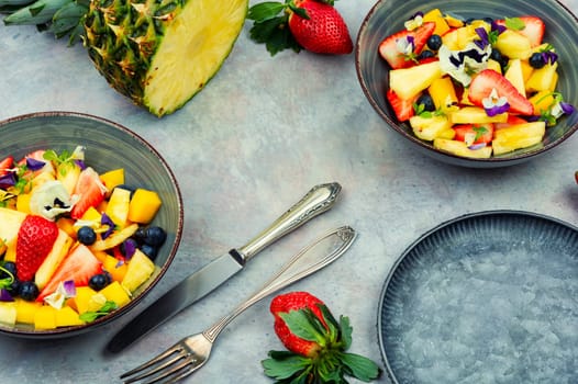 Salad of pineapple, strawberries and berries with edible flowers in a bowl