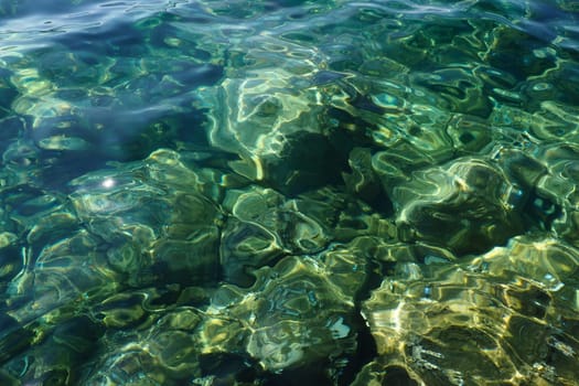 Green azure turquoise blue transparent sea salt water texture. Top view of the water surface and ripples. Water sea waves background. The rocky bottom with algae is visible through the crystal water.
