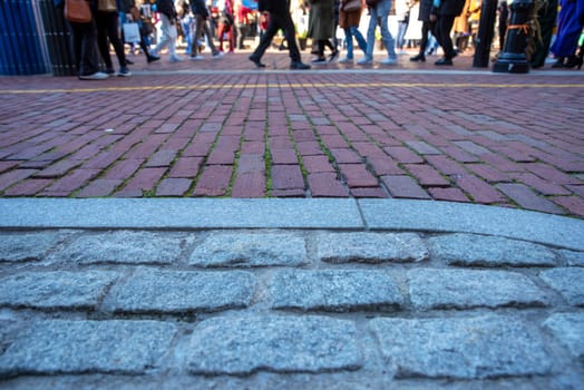 Cobblestone and brick historic street closeup with pedestrian feet crossiing in background with yellow Freedom Trail line visible on bricks. Sunny outdoor day in Boston with copy space.
