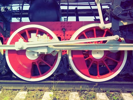 Retro vintage wheels of a locomotive or train close up. Red large heavy metal wheels with piston guiding mechanisms. Locomotive of the 19th - 20th centuries with a steam engine. Retro style.