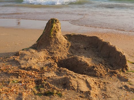 a palace or a house made of sand on a sandy beach. Excavated pit, elevation and seaweed on the roof of the house. Child's vacation at sea. Imagination and fantasy in the creativity of children.