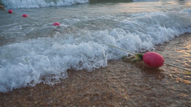 Buoys on a rope near sea water. The buoys are pink restraints to alert people to the depth of the water. Rescue of the drowning. Delimiting a place on a sandy beach between hotels. Wave with bubbles