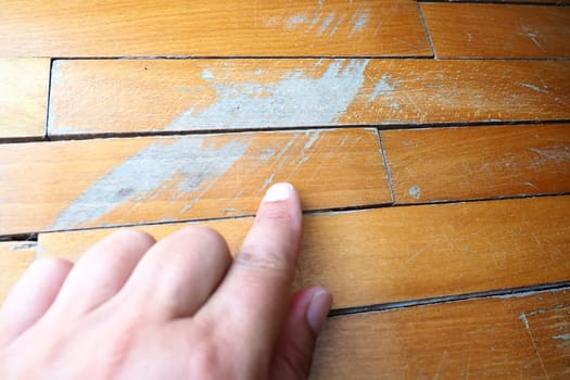 Old, scratched parquet flooring needs maintenance. the parquet is damaged by scratches from prolonged use. Master's hands show damage to the floor.
