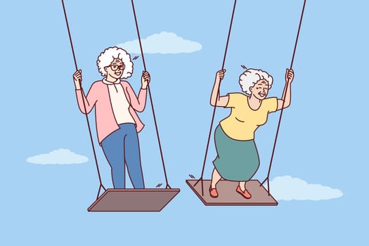 Two elderly women enjoy swinging and enjoying happy old age and not having to go to work. Carefree gray-haired female of retirement age remembers entertainment from youth and does not want to grow old