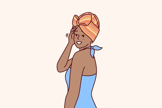 Charming African American woman with traditional turban on head is dressed in blue dress for going to ethnic party. African girl smiling and looking at screen demonstrating fashion national minorities