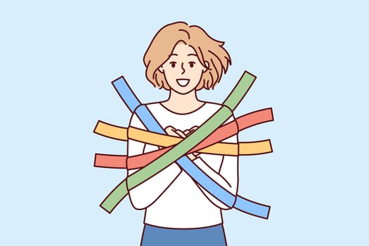 Positive girl smiles happily glued to wall with multi-colored adhesive tapes and is hostage. Metaphor of dependence and limited choice due to positive emotions and lack of critical thinking