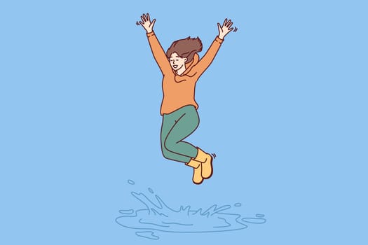 Happy woman jumping in puddle enjoying first autumn rain after hot summer. Girl in good mood in casual clothes jumps standing in puddle, receiving positive emotions from long-awaited walk