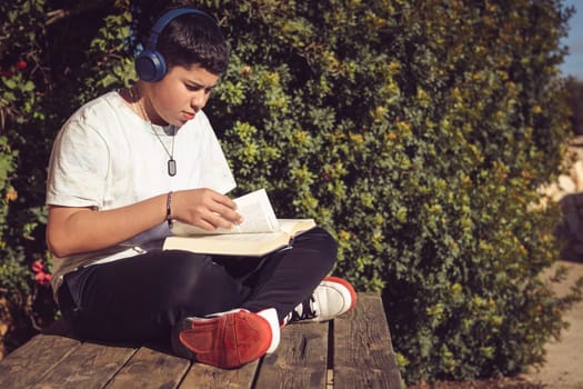 young man turning the pages of the book he is reading, sitting on the wooden bench in the garden of the country house, on the outskirts of the city