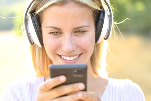 Front view of a happy teen listening to music watching phone content wearing headphone