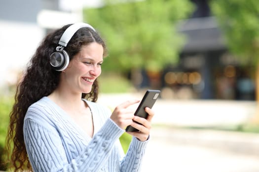 Happy woman in the street listening audio on phone and headphone