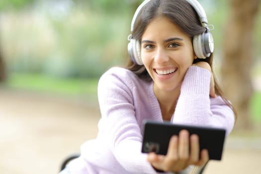 Happy woman looks at you listening to music in a park