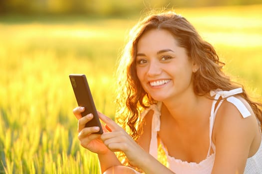 Happy woman posing in a field holding cell phone at sunset