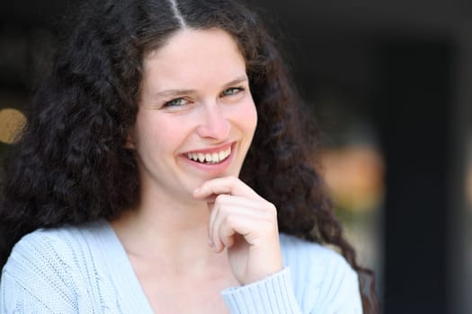 Happy woman smiling with curly hair looking at you in the street