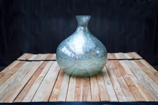 A still life with a blue vase on a stack of wooden slats, against a dark background.