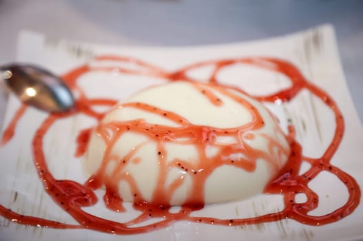 A dessert on a plate, panna cotta with raspberry sauce.