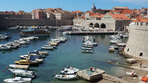 Dubrovnik, Croatia, August 14, 2022. City port in summer, tourist attraction. Tourists walk, get into boats and ships and go on boat trips. Adriatic Sea. A local resident plays with a dog. Old forts