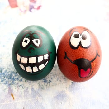 Easter eggs dyed green and brown with painted laughing faces. Funny grimaces with eyes, tongue and big white teeth. Scary face for Halloween. Emoticon for Easter. Light abstract background
