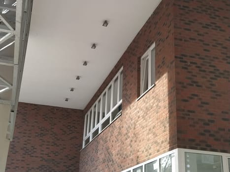 Exterior of the new school. New plastic white windows. Fashionable brown - red facing brick. Metal arch with canopy. Ceiling lighting. School entrance. Serbia, Sremska Mitrovica