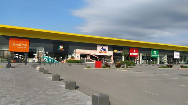 Stop shop shopping center, Sremska Mitrovica, Serbia, June 06, 2022. Square with open shops dm, intersport, dekordom, ccc, lc waikiki. People, parking and pavement. Sunny summer day.