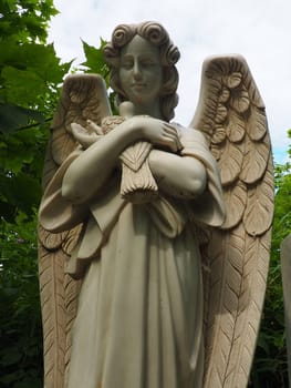 An angel with a dove. Sculpture in the cemetery. The figure of an angel with wings holding a bird in his arms. Lamentation for the deceased. Headstone monument on a Christian grave. Sadness sorrow