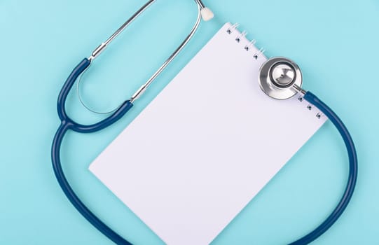 Doctor's Day Concept, Top view, doctor stethoscope and white peper note book diagnosis of heart disease isolated on blue background with copy space, Medical and Health care insurance