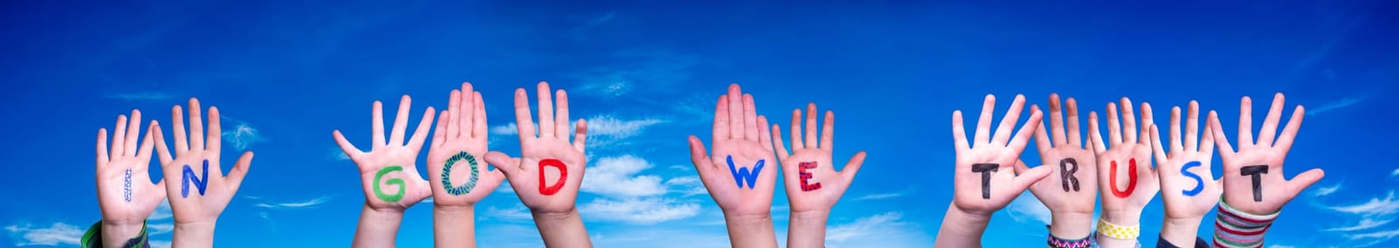 Children Hands Building Colorful English Word In God We Trust. Blue Sky As Background.