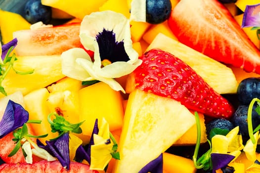 Salad of pineapple, strawberries and berries, decorated with edible flowers.