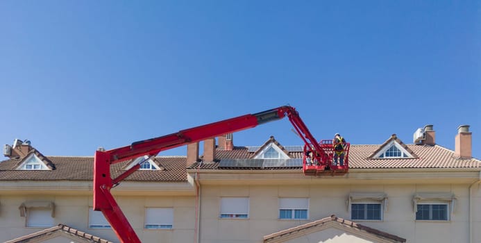 Workmen installing solar panels on the roof of a terraced house. They working over articulated boom lift