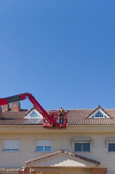 Workmen installing solar panels on the roof of a terraced house. They working over articulated boom lift