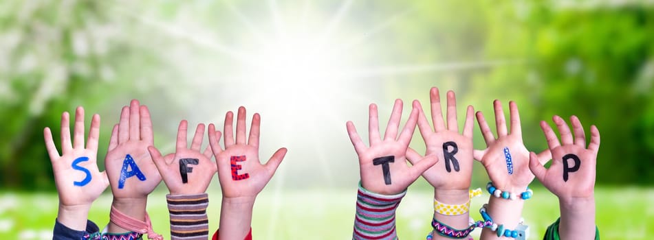 Children Hands Building Colorful English Word Safe Trip. Summer, Sunny Green Grass Meadow As Background