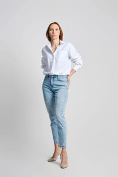 Attractive middle aged woman in white shirt put palms of her hands in back pockets of her blue jeans