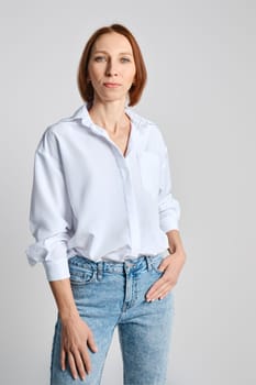 Portrait of confident middle aged woman posing against grey studio background