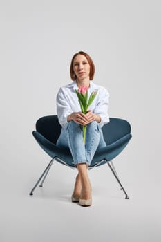Low angle view at middle aged positive woman sitting in armchair with tulips in hand