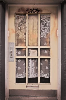 Vertical shot of an old, burnt front door in Essen, Germany with elegant curtains visible behind it