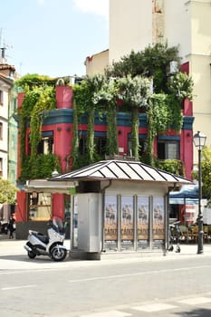 Vertical shot of a kiosk and scooter in front of a building overgrown with vegetation