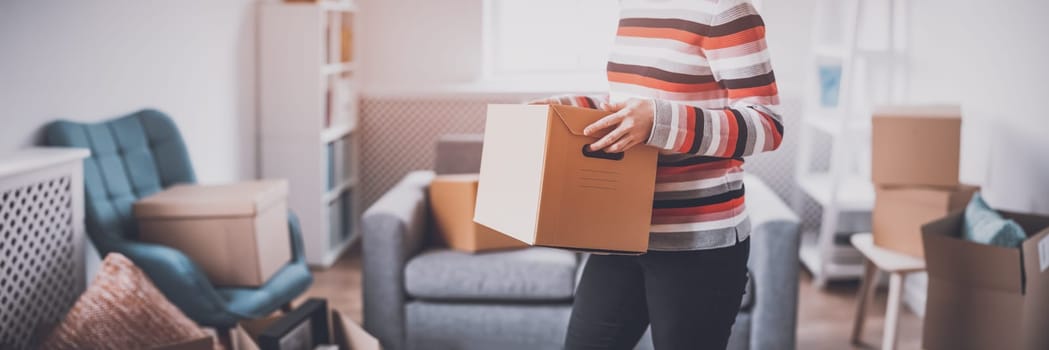Woman carring cardboard box in her hands. Concept of renting, moving in new house and buying an real estate.