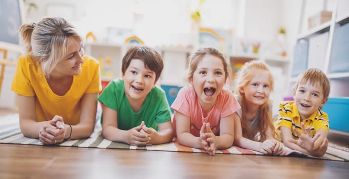 Group of children and teacher lying on the floor and looking in the camera. Concept of relationship, friendship and education.