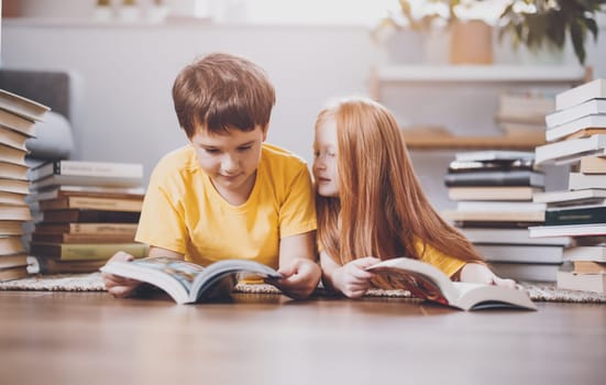 Two cute children lying on the floor indoors with books on the head. Concept of hobby and education.