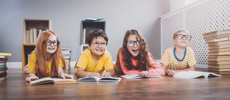 Four cute children in glasses lying on the floor indoors with books. Concept of hobby and education.