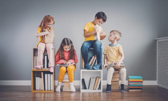 Group of children sitting on the book's stacks and on the bookshelves in the room and reading periodical. Concept of education and friendship.