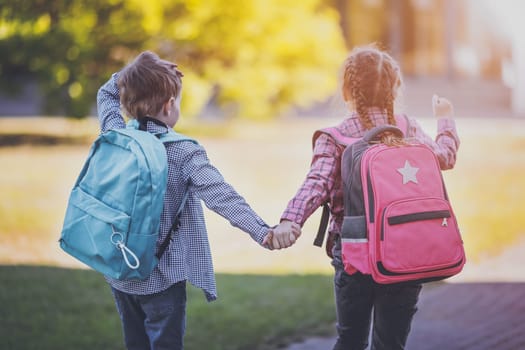 Girl and boy going to the school holding hands to study at it. Concept of back to school and friendship.