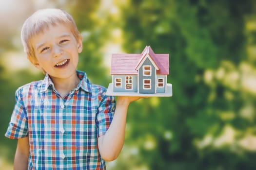 Little child holding in his hand a model of the house. Concept of the family moving to another house, of the real estate, of the financial loan and mortgage.