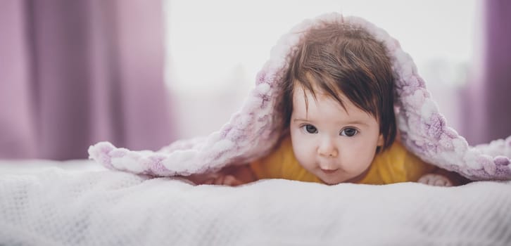 Cute little baby lying under pink blanket. Concept of childhood and maternity.