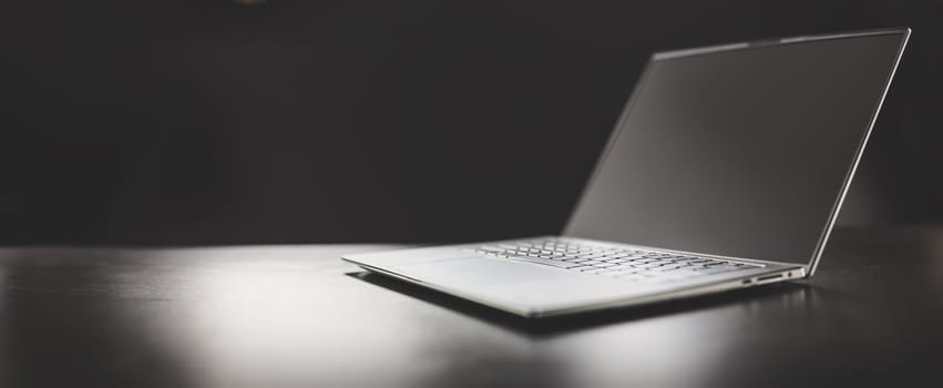 Grey laptop on the dark table on the black background. Concept of the backdrop and banner.