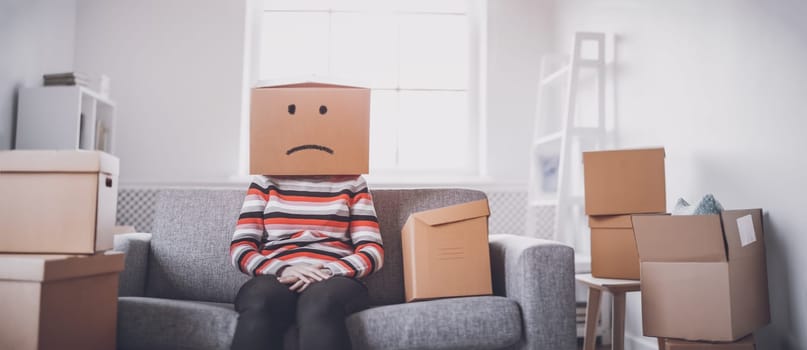 Tired sad woman with cardboard box on her head sitting on the sofa in her new house.Concept of renting, moving in new house and buying an real estate.