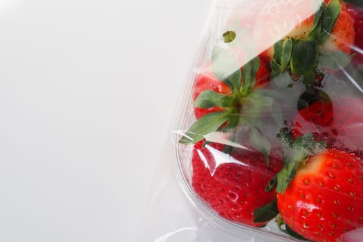 Ripe strawberries in a plastic package on a white background. Delicious fresh berries in a container for sale to customers. Keeping food fresh. Healthy food, vitamins and microelements