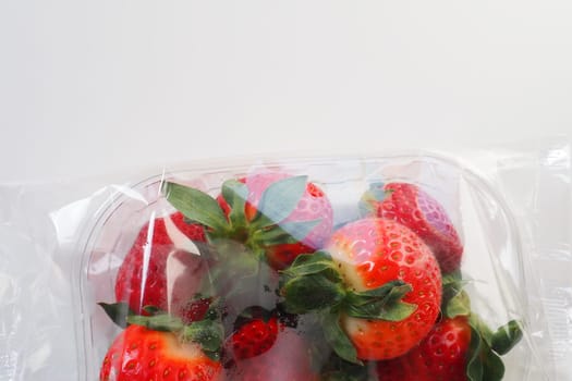 Ripe strawberries in a plastic package on a white background. Delicious fresh berries in a container for sale to customers. Keeping food fresh. Healthy food, vitamins and microelements